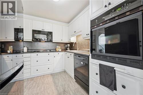 White cabinetry with black hardware, black built-in wall oven, dark tile backsplash, and light-toned flooring - 54 Green Valley Drive Unit# 13, Kitchener, ON 