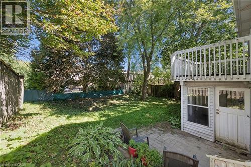 Expansive green space featuring mature trees, a wooden privacy fence, a brick paver patio, an exterior door, and an upper-level balcony with white railings - 512 Thorndale Drive, Waterloo, ON 