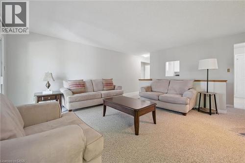 Carpeted living area with light-toned walls, a partial wall with a wood-finish railing, and an architectural opening to another room - 512 Thorndale Drive, Waterloo, ON 
