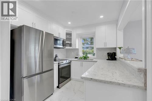 White shaker-style cabinetry with crown molding, stainless steel appliances, speckled stone countertops, a full height backsplash, and recessed lighting - 2435 Coho Way, Oakville, ON 