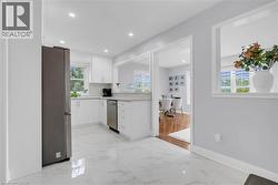 White cabinetry, light-toned countertops, stainless steel appliances, recessed lighting, and white tile flooring - 