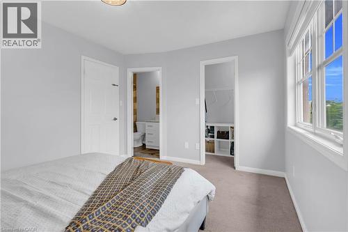 Carpeted flooring with light gray walls, an attached bathroom featuring a vanity and toilet, a walk-in closet with built-in shelving, and a large multi-pane window - 2435 Coho Way, Oakville, ON 