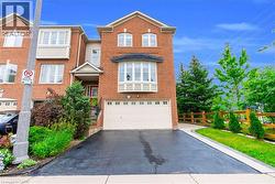 Brick exterior featuring a bay window, an integrated garage, a paved driveway, and mature landscaping - 
