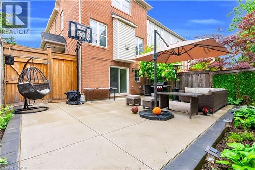 Concrete patio area with brick exterior and privacy fencing, featuring sliding glass doors and layered landscaping - 2435 Coho Way, Oakville, ON 