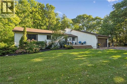 Front exterior featuring white siding, a prominent covered entry, a wood deck, an attached garage, and mature landscaping - 282 Concession Rd 2, Scotland, ON 