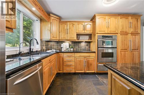 Wood cabinetry with dark countertops, double basin sink with matte black faucet, integrated stainless steel double oven, and dark tile flooring - 282 Concession Rd 2, Scotland, ON 