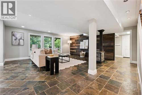Spacious living area featuring large windows, recessed lighting, varied-pattern stone tile flooring, and a wood-paneled accent wall with a freestanding stove - 282 Concession Rd 2, Scotland, ON 