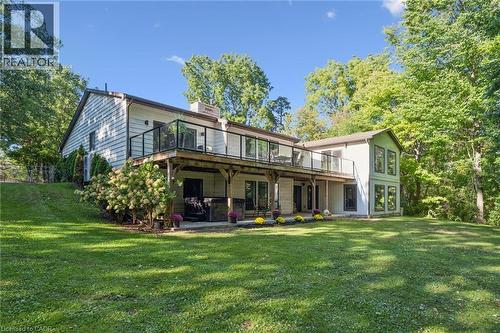 Expansive rear yard featuring a large elevated wood deck with glass panel railing, a covered ground-level patio, and extensive surrounding mature trees - 282 Concession Rd 2, Scotland, ON 