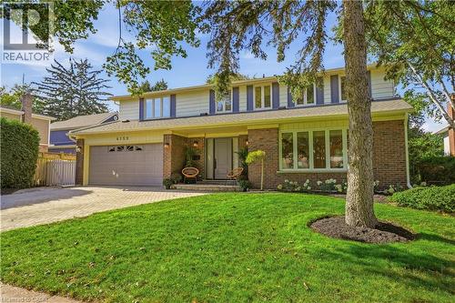 Brick exterior with light siding, front-facing garage with a paver driveway, manicured lawn with mature trees, and a covered front entry - 4159 Spruce Avenue, Burlington, ON 