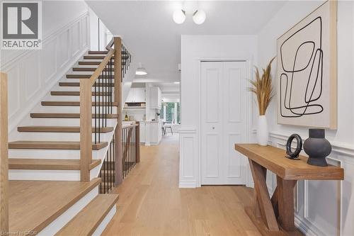 Light wood-finish flooring throughout, staircase with wood treads and metal balusters, wainscoting details, and bi-fold doors - 4159 Spruce Avenue, Burlington, ON 