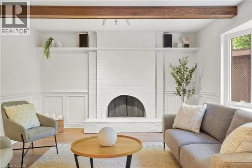 Exposed wood beam, white painted brick fireplace with arched opening, built-in shelving, wainscoting, and wood-finish flooring - 4159 Spruce Avenue, Burlington, ON 