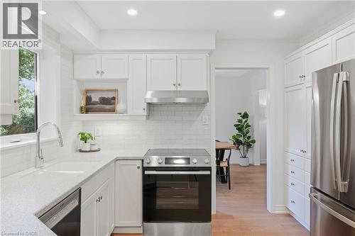 White cabinetry with brushed nickel hardware, stainless steel appliances, light-toned countertops, subway tile backsplash, and recessed lighting - 4159 Spruce Avenue, Burlington, ON 