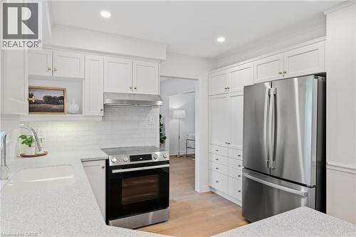 White shaker cabinetry, stainless steel appliances, light-toned wood-finish flooring, undermount sink, and white subway tile backsplash - 4159 Spruce Avenue, Burlington, ON 