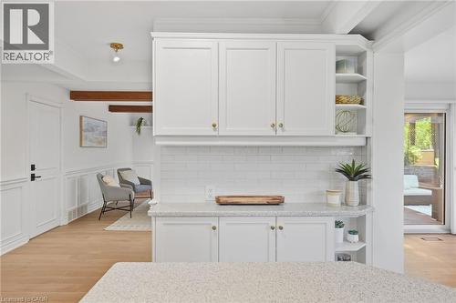 White shaker cabinetry with brass hardware, subway tile backsplash, wood-finish flooring, and exposed wood ceiling beams - 4159 Spruce Avenue, Burlington, ON 