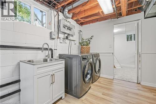 Laundry area with wood-finish flooring, white cabinetry, stainless steel sink, and ample overhead lighting - 4159 Spruce Avenue, Burlington, ON 