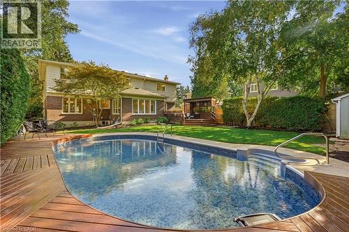 In-ground swimming pool with integrated steps, surrounding wood-finish decking, and a manicured lawn - 4159 Spruce Avenue, Burlington, ON 