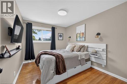 Bright bedroom featuring hardwood flooring, a white built-in platform bed with integrated drawers and nightstands, recessed ceiling lighting, and large window with black-out curtains - 13 Allanburg Road S, St. Catharines, ON 