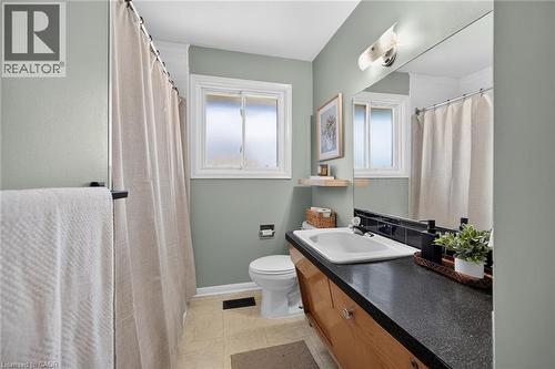 Spa-inspired bathroom featuring soft sage-green walls, dual vanity with wood-finish cabinetry and dark countertop, rectangular vessel sink, chrome fixtures, and bright natural light from dual windows - 13 Allanburg Road S, St. Catharines, ON 