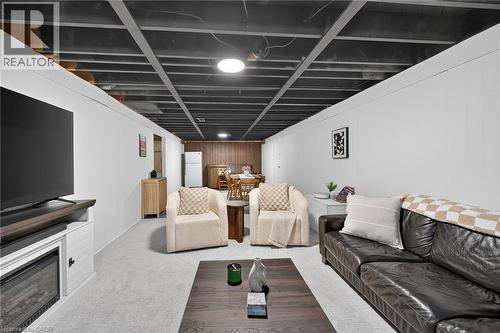Finished lower level featuring a painted open-joist ceiling, light-toned carpeting, white paneling, an integrated electric fireplace, and a wood-paneled accent wall - 13 Allanburg Road S, St. Catharines, ON 