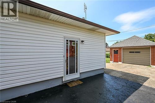 White vinyl siding exterior with a storm door entry, brown gutters, and an exterior light fixture - 13 Allanburg Road S, St. Catharines, ON 
