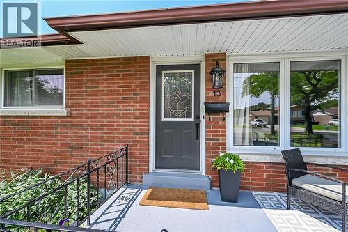Brick exterior featuring a gray entry door with decorative glass, white-framed windows, and a black wrought iron handrail - 13 Allanburg Road S, St. Catharines, ON 