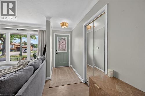Bright entryway showcasing hardwood flooring, a green-painted entry door with decorative hardware, and mirrored closet doors - 13 Allanburg Road S, St. Catharines, ON 
