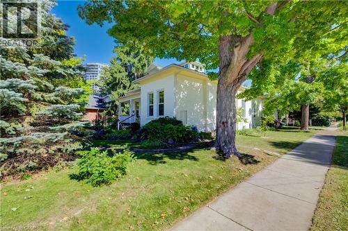White exterior with a covered porch, surrounded by mature trees and established landscaping - 59 Allen Street W, Waterloo, ON 