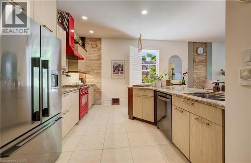 Stainless steel French door refrigerator, red range oven with matching range hood, light wood-finish cabinetry, light-toned tile flooring, and exposed brick accents - 59 Allen Street W, Waterloo, ON 