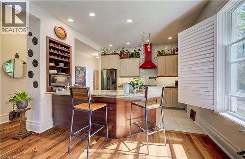 Kitchen featuring a central island with countertop seating, wood-finish flooring, a built-in wine rack, light-toned cabinetry, and a red range hood - 59 Allen Street W, Waterloo, ON 