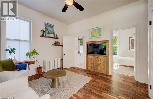 Wood-finish flooring throughout, white painted walls, ceiling fan, white paneled doors, and a built-in media cabinet with wood paneling - 59 Allen Street W, Waterloo, ON 