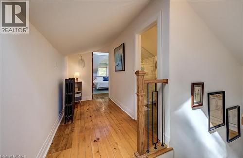 Hardwood flooring with a natural finish, white wall paint, and a wooden stair railing with black metal balusters - 59 Allen Street W, Waterloo, ON 