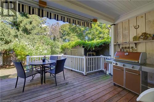 Expansive wooden deck with a retractable striped awning, white railing, wood paneling, and a built-in outdoor cooking station - 59 Allen Street W, Waterloo, ON 