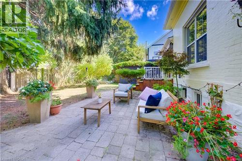 Paved patio area, mature trees, white painted brick exterior, white framed windows, and a raised wooden deck - 59 Allen Street W, Waterloo, ON 
