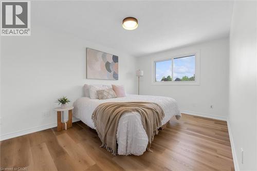 Bedroom featuring wood-finish flooring, a contemporary flush-mount ceiling light, white baseboards, and a window with white trim - 49 Grove Avenue, St. Catharines, ON 