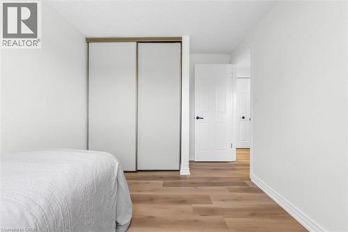 Bedroom featuring wood-finish flooring and a white sliding closet door system with a wood-tone frame - 49 Grove Avenue, St. Catharines, ON 