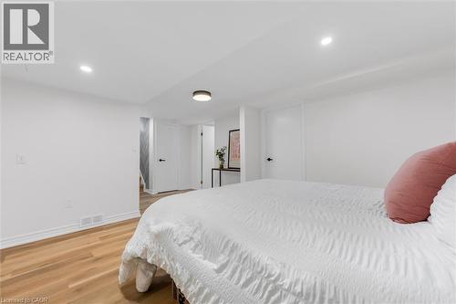 Spacious room featuring light wood-finish flooring, recessed lighting, white baseboards, and white doors with matte black hardware - 49 Grove Avenue, St. Catharines, ON 