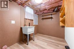 Utility space featuring a freestanding wash tub with exposed plumbing, light wood-finish flooring, and an open unfinished ceiling - 