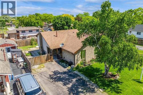 Stone veneer exterior with a brown shingle roof, mature front yard tree, paved driveway, and fenced rear yard - 49 Grove Avenue, St. Catharines, ON 