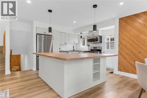 Kitchen featuring a central island with wood-finish countertop, light-toned cabinetry, stainless steel appliances, and wood-finish flooring - 49 Grove Avenue, St. Catharines, ON 