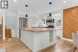 Kitchen featuring a central island with wood-finish countertop, light-toned cabinetry, stainless steel appliances, and wood-finish flooring - 
