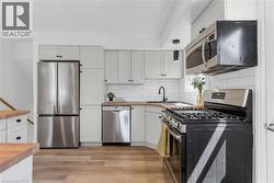 Contemporary kitchen featuring light-toned cabinetry, wood-finish countertops, stainless steel appliances, a subway tile backsplash, and light wood-finish flooring - 