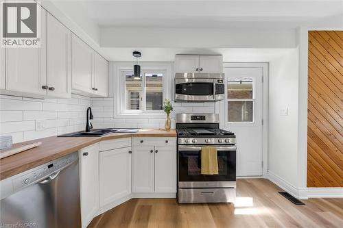 Kitchen featuring wood-finish flooring, white cabinetry, wood countertops, a black sink, and stainless steel appliances - 49 Grove Avenue, St. Catharines, ON 