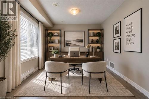 Dedicated home office featuring built-in shelving with wood-finish backing, a spacious desk with integrated storage, and two upholstered chairs - 212 Ellen Davidson Drive, Oakville, ON 