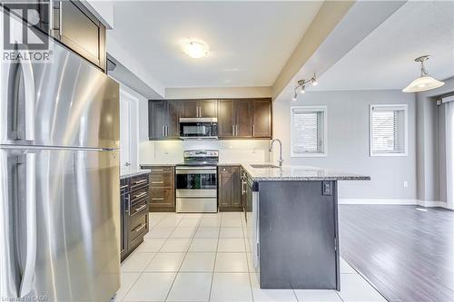 Kitchen featuring stainless steel appliances, dark wood-finish cabinetry, granite-finish countertops, and white tile flooring - 212 Ellen Davidson Drive, Oakville, ON 