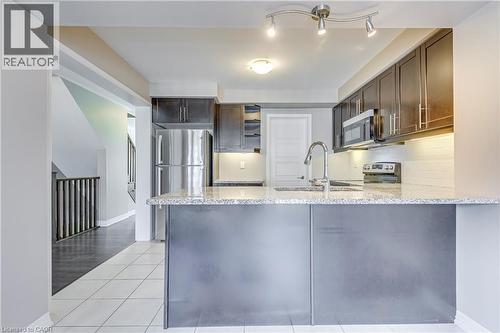 Kitchen featuring a stainless steel refrigerator, dark wood-finish cabinetry, a large kitchen island with a stone countertop, and integrated stainless steel appliances - 212 Ellen Davidson Drive, Oakville, ON 