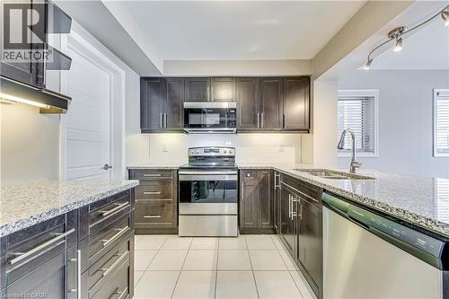 Kitchen featuring dark wood-finish cabinetry, light-toned granite countertops, and stainless steel appliances - 212 Ellen Davidson Drive, Oakville, ON 