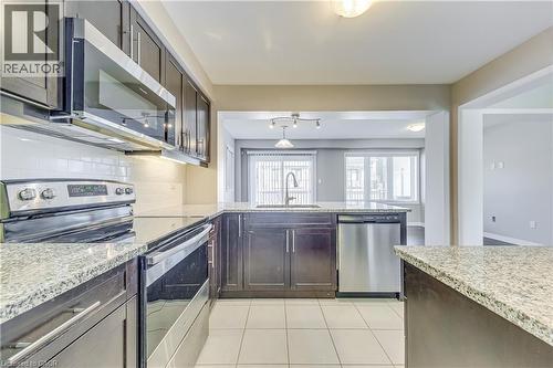 Kitchen featuring dark wood cabinetry, light granite-style countertops, stainless steel appliances, a white subway tile backsplash, and white floor tiles - 212 Ellen Davidson Drive, Oakville, ON 