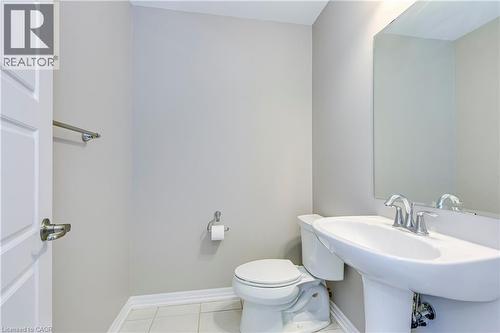 Pedestal sink with chrome fixtures, wall-mounted mirror, white toilet, and light-colored tile flooring - 212 Ellen Davidson Drive, Oakville, ON 