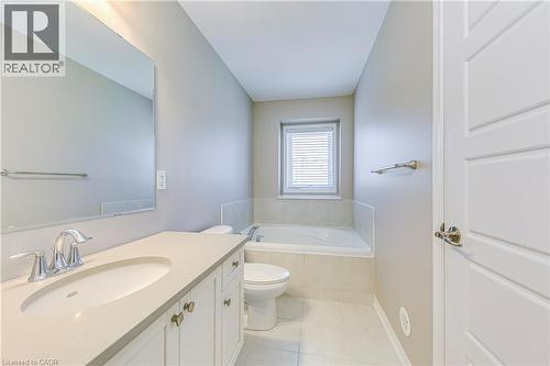 Vanity with an integrated sink and chrome faucet, large rectangular mirror, soaking tub with tiled surround, and a single window with blinds - 212 Ellen Davidson Drive, Oakville, ON 