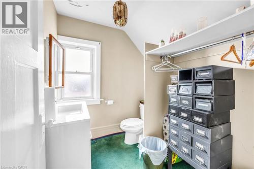White vanity with an integrated sink, a single-pane window, white toilet, ceiling-mounted light fixture, and a built-in closet with shelving and a hanging rod - 414 Main Street E, Hamilton, ON 
